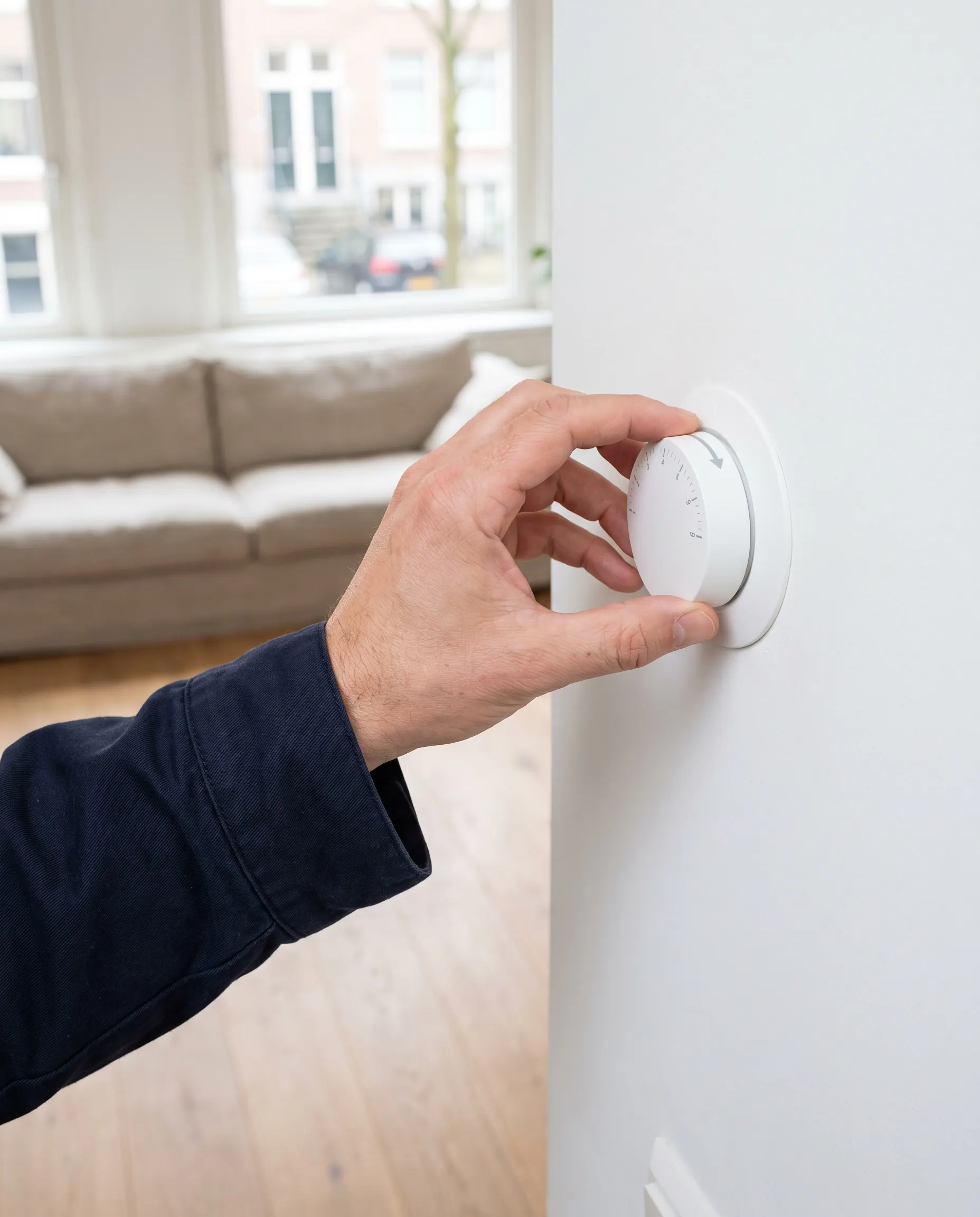 Hand draait een ronde thermostaat aan de muur lager